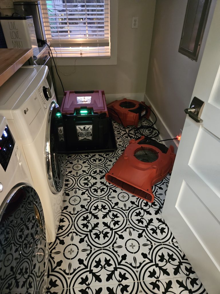 Laundry room featuring a washing machine, drying equipment, and a large red drying fan on a patterned floor, indicating water damage remediation.