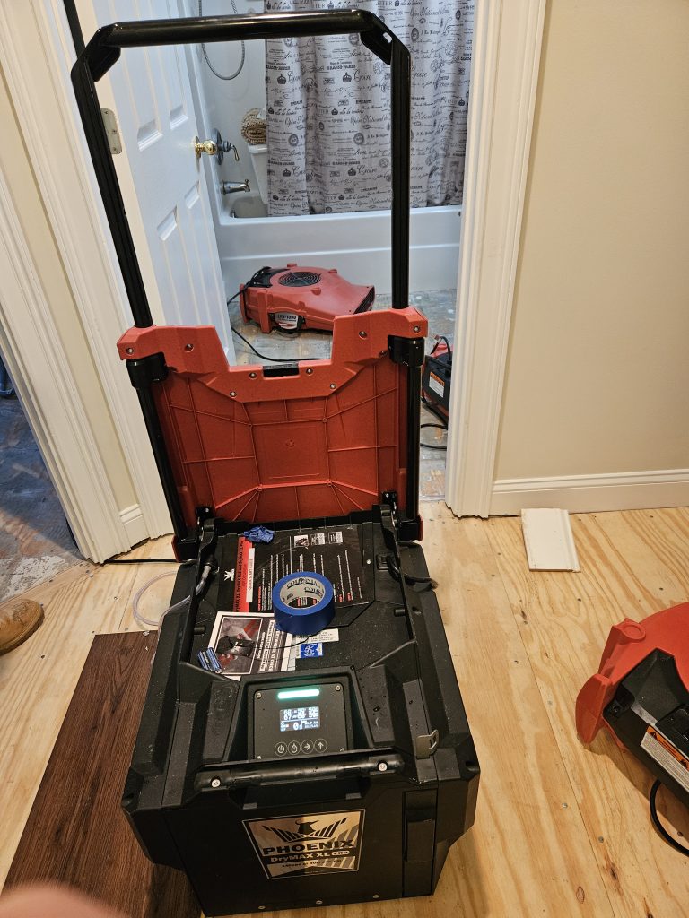 Open tool box displaying digital controls and interior contents, set in a home renovation context with a visible bathroom in the background.