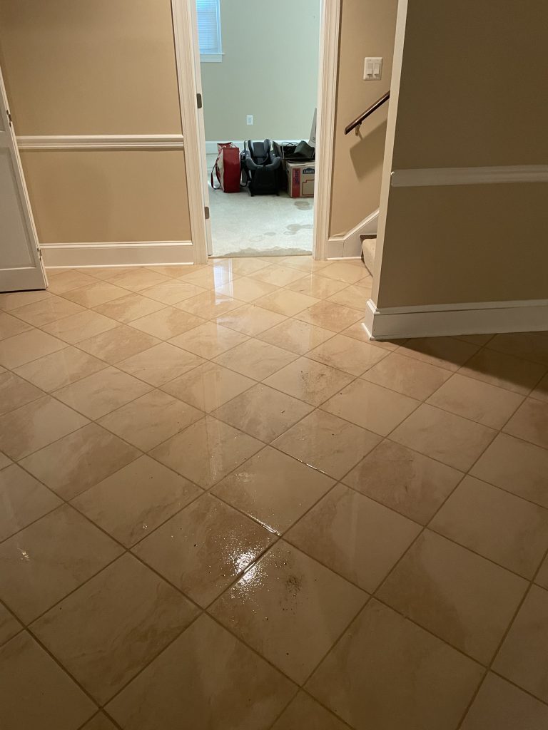 Wet tile floor in a hallway, leading to a room with bags and boxes, indicating potential water damage or recent cleaning.