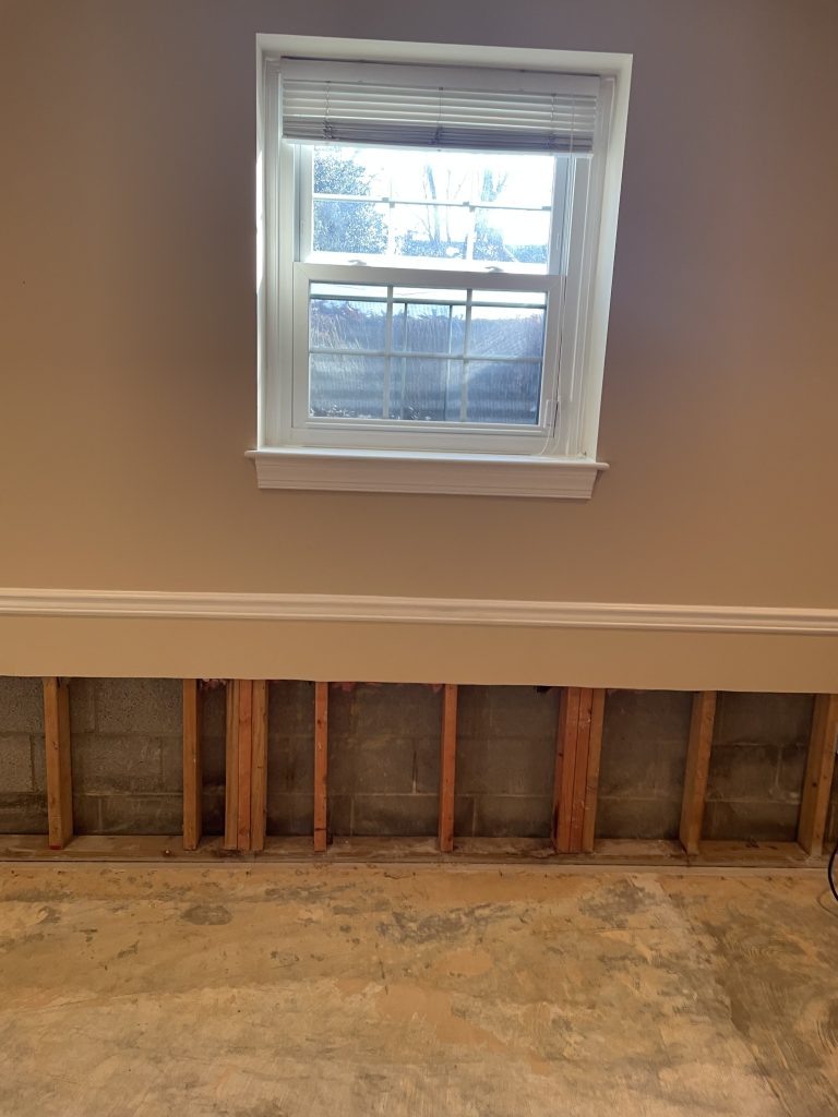 Renovation in progress: a window with blinds above exposed framing and cinder block wall, showing unfinished wall and flooring.