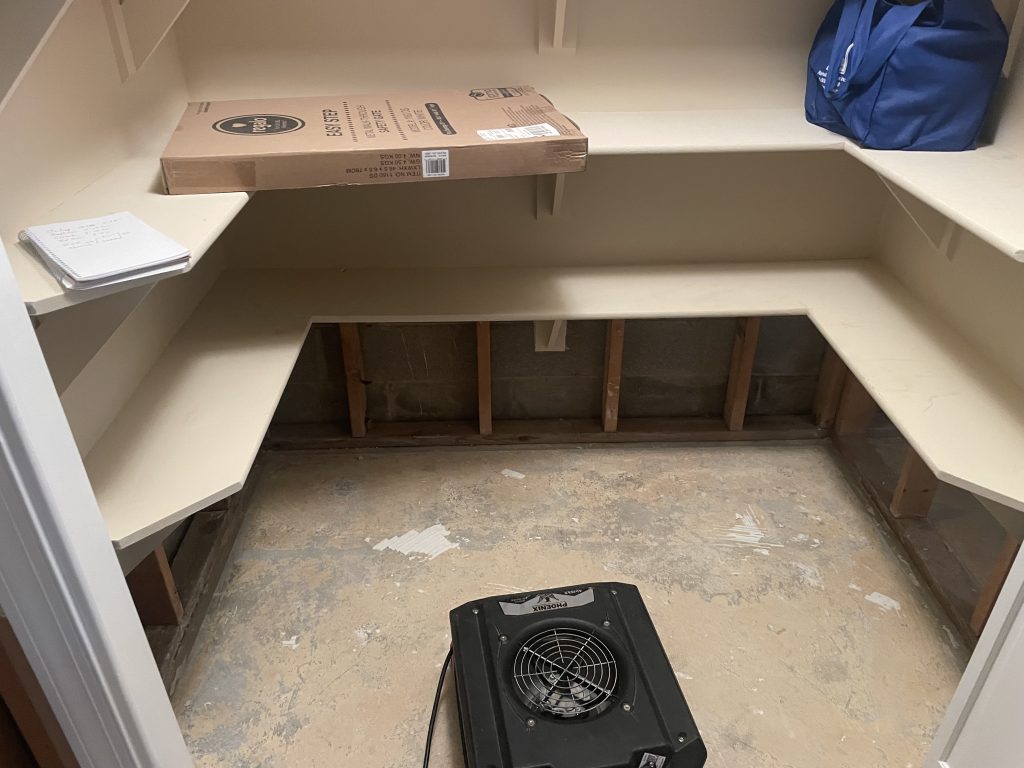 Empty closet with shelves, a box, a notebook, and a fan on the floor, indicating a space possibly undergoing cleaning or renovation.