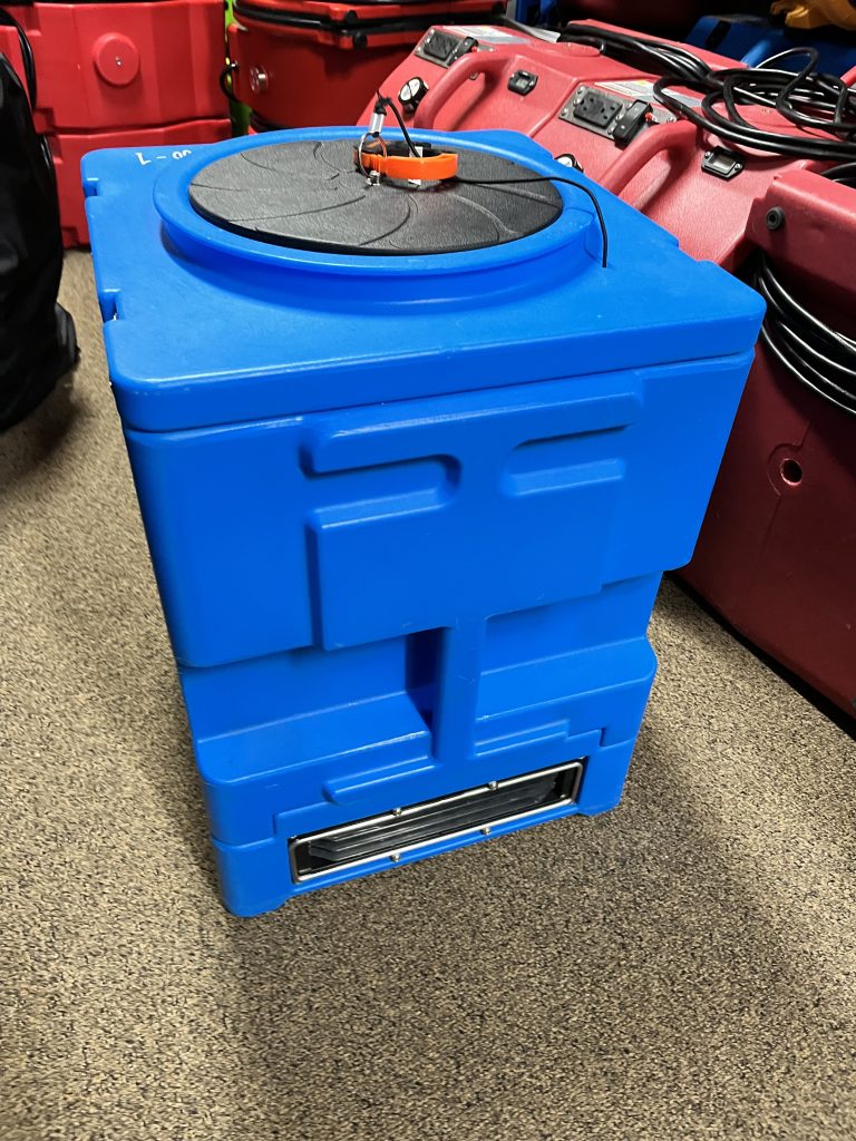 Blue storage container with a circular lid, featuring an orange handle and various wires. Located among several red containers in a storage area.