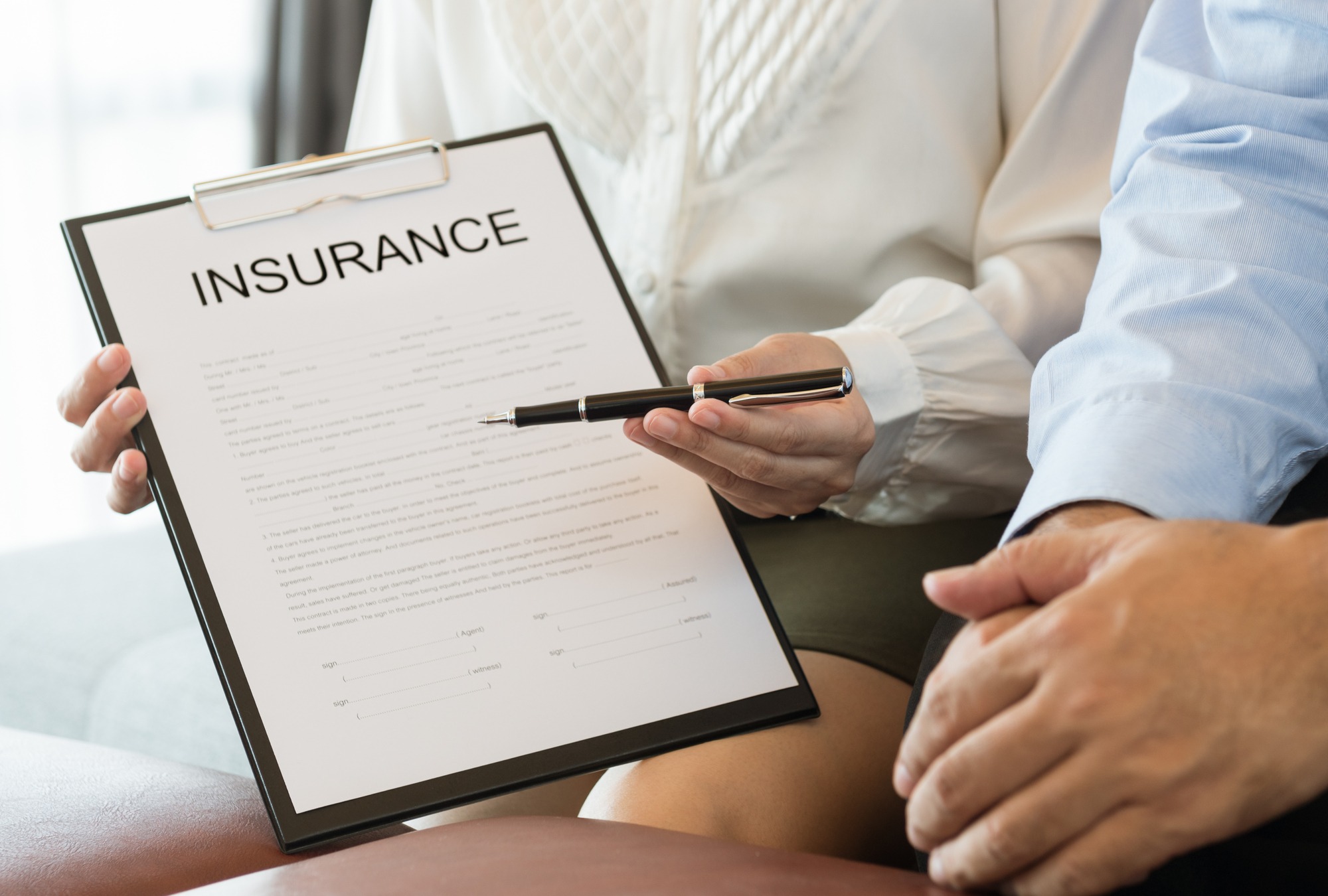 A person holding an insurance document and a pen, showing the contract to another individual, suggesting a discussion about policy details.
